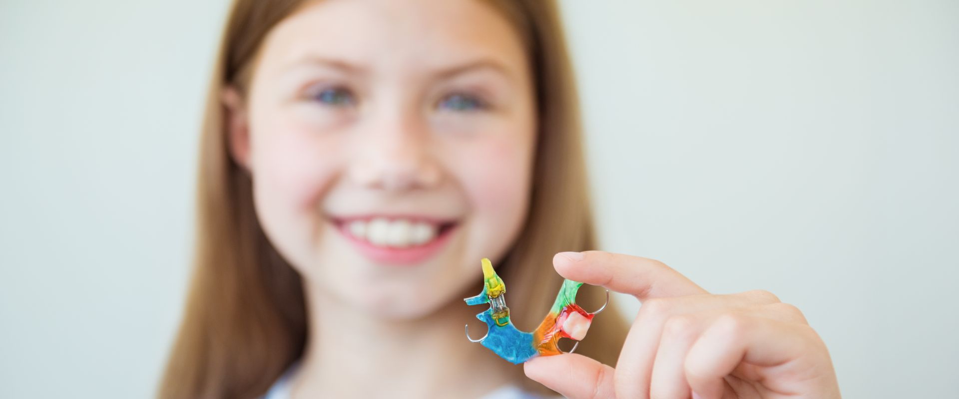 Lächelndes Kind mit loser Zahnspange in der Hand